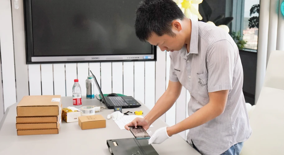 A worker wearing white gloves reviewing an industrial panel on a preparation table.
