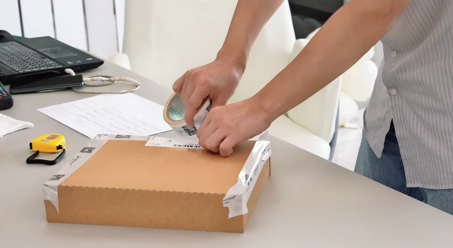 Hands sealing a cardboard shipping box at an order preparation desk.