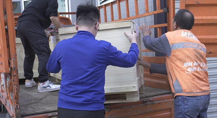 Workers moving a wrapped package into a small delivery truck.