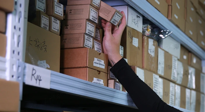 A hand retrieving a labelled box from a warehouse shelf.