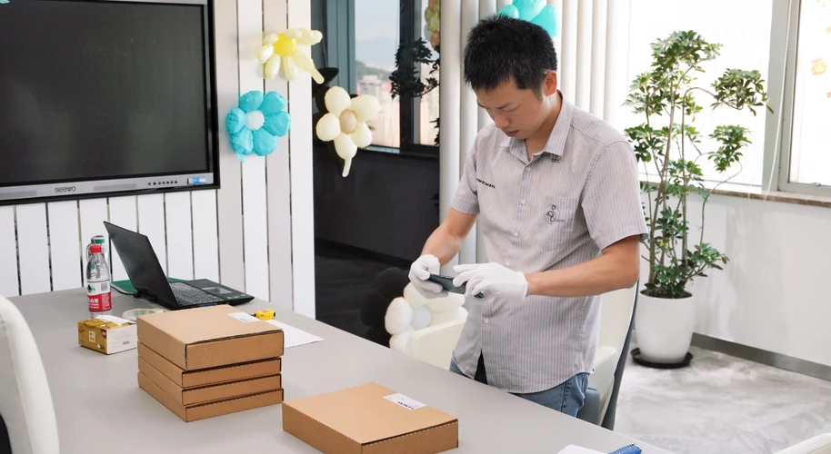 A worker wearing white gloves handling a component beside stacked packing boxes.